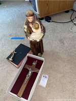 Photo of religious figurine of saint holding child, two crosses (one wooden crucifix in box, one smaller cross on box) on carpet floor