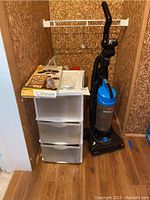 Photo showing Bissell PowerForce vacuum cleaner standing next to white three-drawer plastic storage unit with translucent drawers inside a small closet.