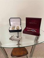 Geneva Quartz watches in black box, Trademark Twelve watch in red box, blue pen, and metal pocket tool on glass table