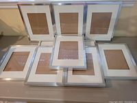 Group layout of all 10 silver-toned IKEA picture frames arranged together on a table showing front view with white matting inside.