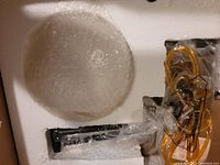 Top view of a lamp part and wiring wrapped in bubble wrap and plastic inside protective foam packaging.