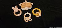 Three wooden teethers and one wooden toy camera placed on black background, shown to detail shape and color of each item.