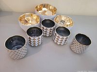 Five decorative painted planters: three cylindrical with black interior and gold geometric pattern, two multifaceted with gold interior and geometric shapes on the exterior.