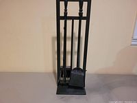 Photo showing the full iron fireplace tool set including poker, brush, shovel all housed in the rectangular iron stand.