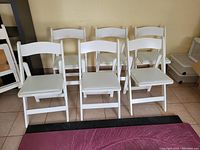 Front view of six white wooden folding chairs aligned in two rows, showing overall condition and some paint wear.