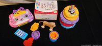 A variety of toddler and infant toys including a soft cat face purse, wooden pull toy, plastic toys, and plush stacking rings