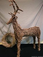 Side view of the grapevine woven reindeer with the rustic wreath on the floor behind it, showcasing the full height and length of the reindeer and the round shape of the wreath.