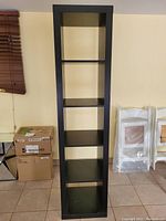 Front view of the Ikea dark wood finish cube bookshelf showing five evenly spaced shelves and overall tall and narrow design