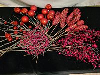 Photo of mixed red artificial berry stems and red pine cone stems grouped together on a dark background.