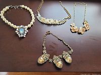 Four necklaces laid out on dark surface showing their overall design and size.