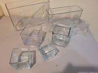 Seven clear glass vases arranged on a flat surface showing various square and rectangular shapes and sizes.
