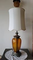 Full view of the amber glass table lamp with white fabric shade, showing the entire piece and scale.