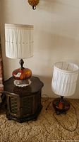 Two amber glass globe and brass table lamps side by side, one on a wooden end table and the other on the floor. Both have white pleated fabric shades.