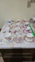 Photo showing multiple bone china tea cups and saucers in various floral designs with one cup marked by green tape.