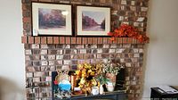 Two framed autumn landscape pictures on mantel above fireplace, with artificial floral arrangements and decor on mantelpiece