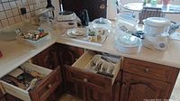 General overview of kitchen drawers and countertop showing various kitchenware including bakeware, cutlery, mixing bowls, cookie cutters and tea service tray.