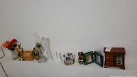 Wide shot showing all items in the lot aligned on a surface against a white wall. Includes vases, oil lamp, jewelry box, figurines, floral items, musical teapot.