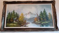 Full view of framed oil painting showing a mountain, lake, trees, and cabin in the foreground.