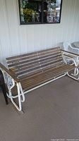 Full view of wooden slat patio swing bench with white metal frame and veranda background