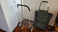 White metal folding cart and plaid fabric shopping trolley side by side on carpeted floor near white door