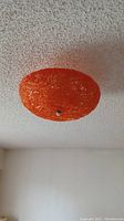 Orange textured spaghetti lamp shade mounted on ceiling showing woven pattern and metal center fixture