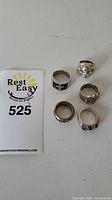 Five sterling silver rings displayed on a white surface with a lot number card.