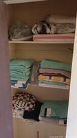 Photo of shelves containing folded assorted towels and linens stacked in multiple colors and patterns, and a compact scale with a furry fabric item on top.