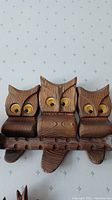 Close up of triple carved owl wall art mounted on branch with hooks underneath