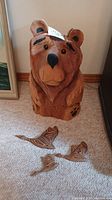 Front angled view of the carved wood bear standing next to two smaller carved wooden geese on carpeted floor.