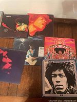 Full view showing 6 Jimi Hendrix vinyl record album covers arranged on wood surface, details of cover art visible.