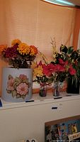 Four artificial flower arrangements in various decorative vases and the hand-painted umbrella stand with 3D floral design on a windowsill.