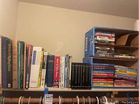 Shelf showing assorted books including encyclopedias and DVDs stacked in a box to the right.