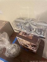 Three silver metal candle holders in clear packaging tied with a silver ribbon, showing pearl and bead decoration.