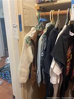 Lot of children's clothing hanging on a rack including a white handknit sweater, brown vest, and other shirts