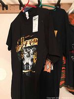 Two black ZZ Top t-shirts hanging on hangers displaying skull and rose graphics along with the band name across the chest.
