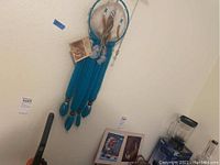 View of large turquoise leather dreamcatcher with feather decorations hanging on wall. Native American lithographs partially visible below.