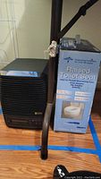 Photo showing black PureAir air purifier and boxed Medline raised toilet seat on floor with metal railing behind.