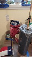 Photo showing the tall smoky gray glass vase, tin coffee can with assorted Koozies, small Texas and American flags, and a coffee mug