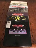 View of 7 stacked Aerosmith vinyl albums showing title 'Rocks' on front album and other album spines visible