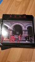 Photo showing Rush album 'Moving Pictures' front cover with people carrying paintings in front of arch.
