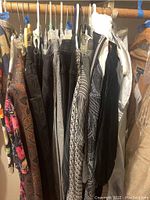 Photo showing several clothing items hung on a rack including floral skirts, striped and checkered pants, and patterned jackets.