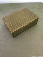 Rectangular metal cigar box with lined Art Deco pattern and closed lid shown from a top angle.
