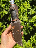 Front of knife in original leather sheath with visible rivets and leather wear