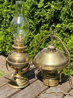 Pair of antique brass lighting items on a wooden surface with outdoor greenery background