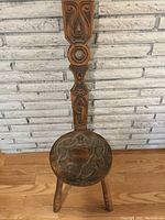 Front view of the antique wooden chair with carved Celtic patterns on the seat and backrest, showing three legs.