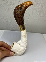 Side view of the antique meerschaum pipe showing the eagle head detailed carving and white claw base held by a hand for scale.