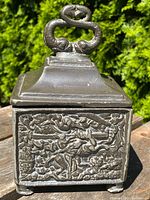 Front and one side view show detailed relief of cherubs and animals on the metal surface and the serpent shaped lid handle.