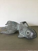 Side view of fish fountain showing detailed scales, fins, and patina
