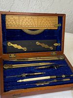 Overview of antique protractor set in open wooden box showing instruments arranged neatly on blue velvet background.
