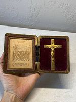 Opened antique brass travelling prayer box showing the printed prayer on left side and crucifix on right side.